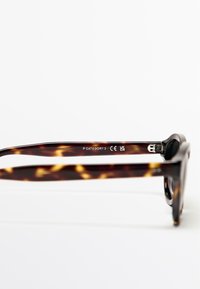 Zonnebril met schildpadprint en glanzende afwerking, voorzien van dikke brilarmen en gegraveerde CE-markeringen. Categorie 3 UV-bescherming aangegeven op het montuur.