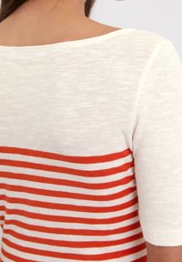 Suéter de crema con rayas anaranjadas horizontales en la mitad inferior, fabricado con un tejido suave y con textura y un escote amplio.