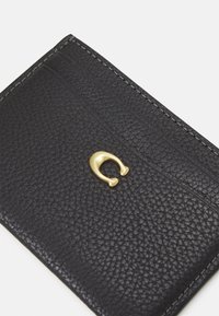 Black leather wallet with a textured surface, featuring a gold hardware accent in the shape of a C. Stitched edges in a contrasting color.