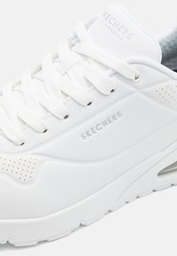 Baskets blanches de Skechers avec une tige synthétique lisse, des lacets plats, des accents perforés et un logo en relief sur le côté.
