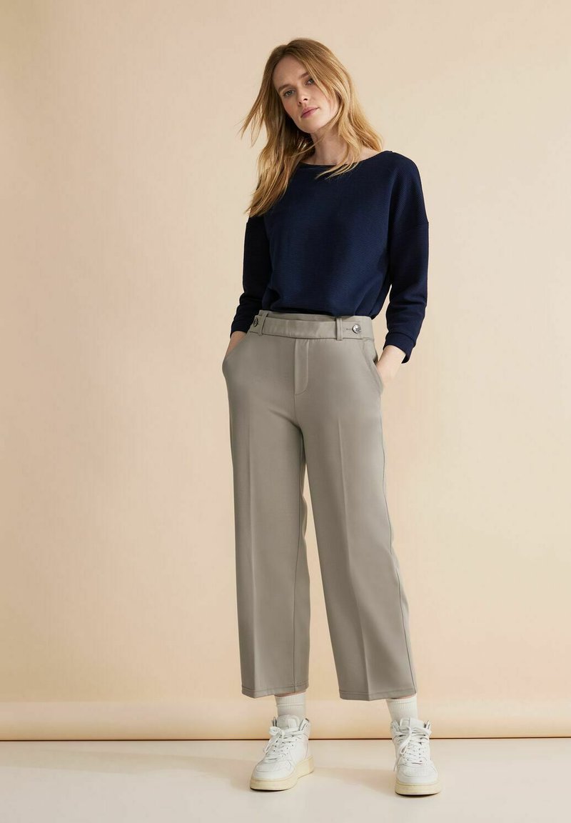 Marinblå tröja med avslappnad passform, parat med ljusgrå vida byxor med bälteshällor och sidfickor. Vita sneakers fulländar looken.