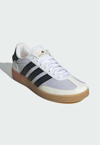 White athletic shoe with black stripes, mesh panels, and a rubber sole. Features a cushioned collar and lace closure.