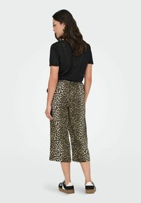 Pantalon culotte imprimé léopard en beige et noir, doté d'une coupe large, d'une taille élastique, et porté avec un t-shirt noir et des baskets.