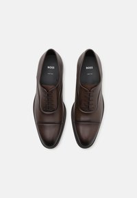 Scarpe eleganti in pelle marrone con finitura liscia, punta rotonda, design con lacci e cuciture tonali sottili, dotate di suola in gomma.