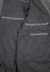 Black quilted jacket interior featuring two zippered pockets and two slip pockets with gray accents. Smooth, padded texture and diamond pattern.