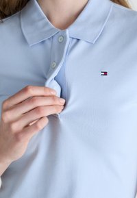 Lyseblå polo-shirt med teksturert stoff, som har krage og stolpe med to knapper, prydet med en liten merkevarelogo.