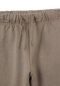 Pantalones de chándal marrones con una cinturilla elástica y cordones ajustables, hechos de una tela suave y texturizada. La vista en primer plano se centra en la cintura.