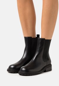 Bottes basses en cuir noir avec panneaux latéraux élastiques, bout rond et petit talon. Texture lisse avec une languette à l'arrière pour un enfilage facile.