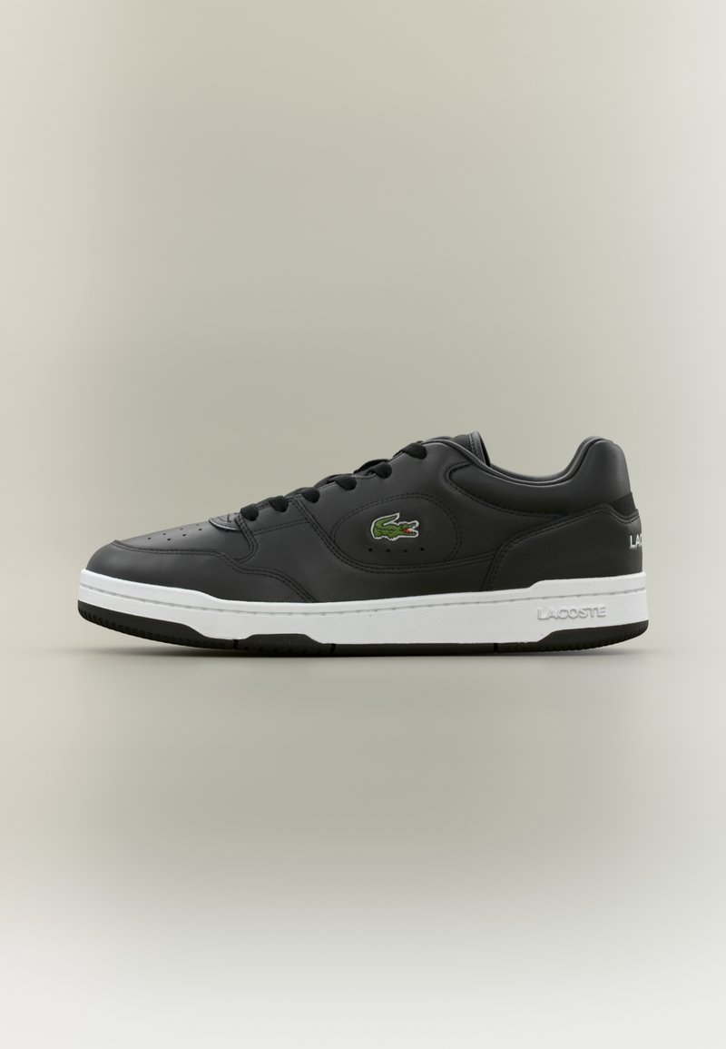 Baskets basses en cuir noir avec semelle blanche, lacets noirs et logo crocodile vert Lacoste sur le côté.