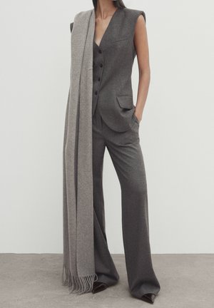 Femme portant un gilet sans manches gris avec un pantalon large assorti et une longue écharpe gris clair drapée sur une épaule.