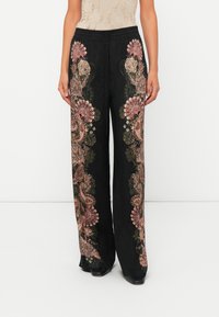 Black wide-leg trousers with pink and beige floral embroidery along the front legs, worn with black pointed shoes and a beige textured top.
