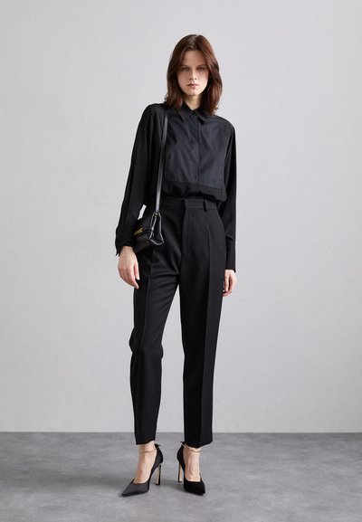 Black cropped shirt with a pointed collar, paired with high-waisted black trousers and pointed black heels. Minimalist design, smooth texture.