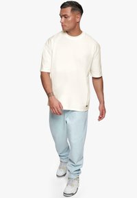 Kremowy t-shirt z krótkim rękawem o luźnym kroju, zestawiony z jasnoniebieskimi dżinsami i szarymi trampkami. Prosty design, bez wzorów czy dodatków.