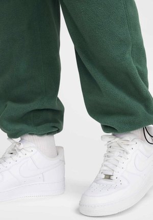 Grønne fleece joggere med manchetter ved anklerne, parret med hvide Nike sneakers og rullede hvide sokker. Joggerne har en blød tekstur.