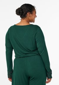 Skakalec z dolgimi rokavi v temno zeleni barvi, z oblo okroglo izrezom in čipkastimi poudarki na manšeti. Gladek material z ohlapnim krojem.