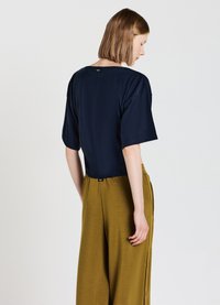 Top blu navy a maniche corte con scollo rotondo, texture liscia e cucitura centrale sul retro. Abbinato a pantaloni larghi color verde oliva.