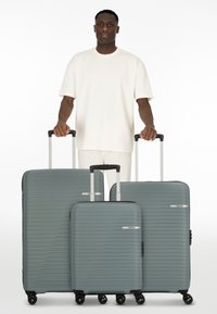 Trois valises rigides avec une finition grise texturée et un design rayé. Chacune est équipée d'une poignée rétractable et de quatre roues pour faciliter le déplacement.