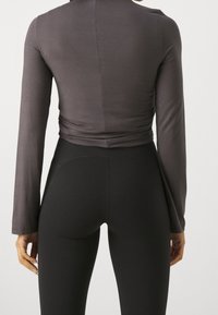 Dark gray long-sleeve top with a fitted design, featuring gathered detail at the waist. Paired with black high-waisted leggings.