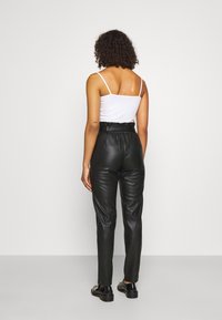 Pantalon taille haute en simili cuir noir avec une coupe fuselée et une ceinture assortie, associé à un simple débardeur blanc.