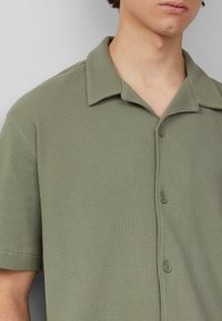 Korte mouwen, olijfgroene overhemd met knopen, gemaakt van een gestructureerde stof met een subtiele ribbelpatroon en een kraag.