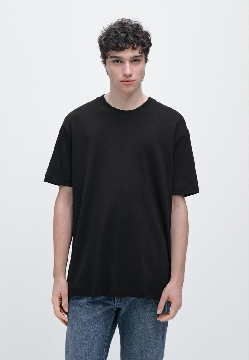 Black short-sleeve T-shirt made of soft cotton, featuring a round neckline and a relaxed fit. Worn with blue denim jeans.