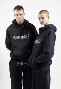 Navy blue hoodie and sweatpants set, featuring a zip-up front, large pockets, and silver "wasted" graphic on the chest and pants. Cotton blend material.