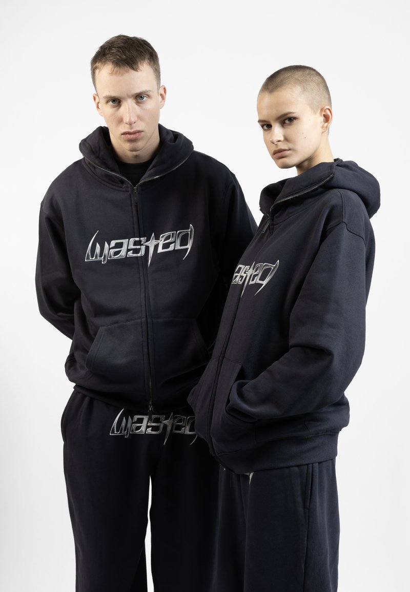 Navy blue hoodie and sweatpants set, featuring a zip-up front, large pockets, and silver "wasted" graphic on the chest and pants. Cotton blend material.