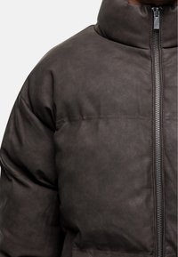 Veste matelassée marron foncé avec un col haut, fermeture éclair apparente et motif matelassé. Fabriquée avec un extérieur texturé et lisse.