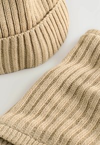 Gestricktes Beanie- und Schalsatz in hellbeige, mit gerippter Textur und weichem Stoff. Beide Teile zeigen ein konsistentes Wellenmuster.
