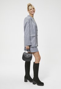 Szary żakiet i spódnica, kozaki za kolano z czarnego zamszu na słupkowym obcasie oraz mała czarna torebka z zapięciem na zatrzask. Gładkie faktury.