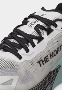 Κοντινό πλάνο λευκού και γκρι αθλητικού παπουτσιού The North Face με μαύρα κορδόνια και υφασμάτινες λεπτομέρειες με υφή στο πάνω μέρος και στην σόλα.