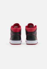 Een paar zwart-rode hoge sneakers met witte tussenzolen, weergegeven vanaf de achterkant op een witte achtergrond.
