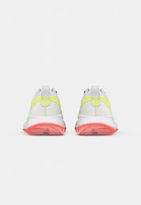 Chaussures de sport blanches avec des accents jaune fluo, des semelles roses et une tige texturée. Possède un col rembourré et une languette arrière en boucle pour un enfilage facile.