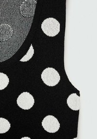 Top nero in maglia con grandi pois bianchi, scollatura rotonda e una texture morbida. Il design include pois di diverse dimensioni e forme.