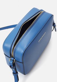 Borsa a tracolla in pelle blu fiammata con zip dorata parzialmente aperta e logo dorato Emporio Armani sul davanti.