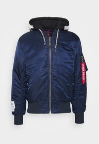 Blouson bomber bleu marine avec capuche noire, fermeture éclair à l'avant, poignets côtelés et étiquette rouge sur la fermeture éclair de la manche gauche.