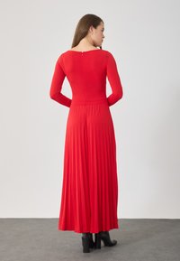 Rode langemouwen jurk met een aansluitende lijfje en geplooide rok, voorzien van een ritssluiting aan de achterkant. Glad materiaal, enkel-lang en met een ontspannen pasvorm.