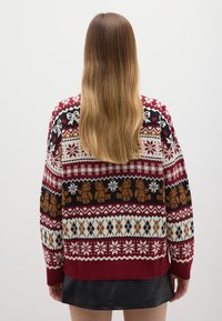 Red and white festive sweater featuring snowflake and bear patterns, knitted design, long sleeves, and a ribbed hem.