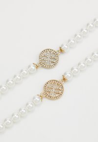 Dva náramky z perlových korálků s kulatými zlatými sponami zdobenými malými jasnými krystaly na bílém pozadí.