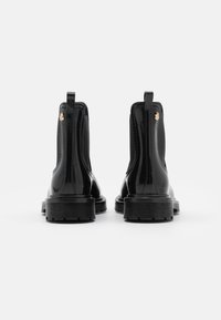 Botines de charol negro con paneles laterales elásticos y tirador, con una suela de goma negra gruesa y detalle del logotipo dorado.