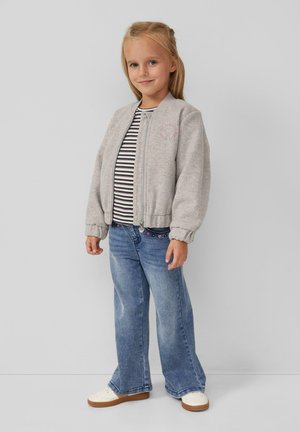 Veste bomber grise avec des poignets côtelés, assortie à une chemise rayée, un jean bleu évasé et des baskets blanches avec des semelles marron.