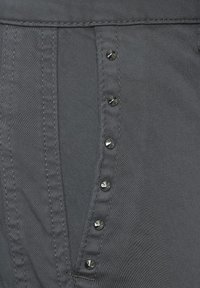 Grå denimtyg med en vertikal rad av metalliska svarta knappar längs sidan, med synliga sömnadsdetaljer.