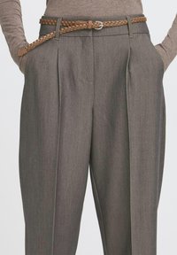 Grau maßgeschneiderte Hose mit zwei vorderen Falten, einer strukturierten Oberfläche und einem geflochtenen braunen Leder-Gürtel mit einer runden Schnalle.