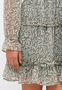 Short-sleeve dress in green with white leaf print. Features ruffled accents along the hem and sleeves, made from lightweight, textured fabric.