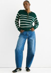 Green and white striped knit sweater with a henley neck and button detail, paired with loose blue jeans and black sneakers.