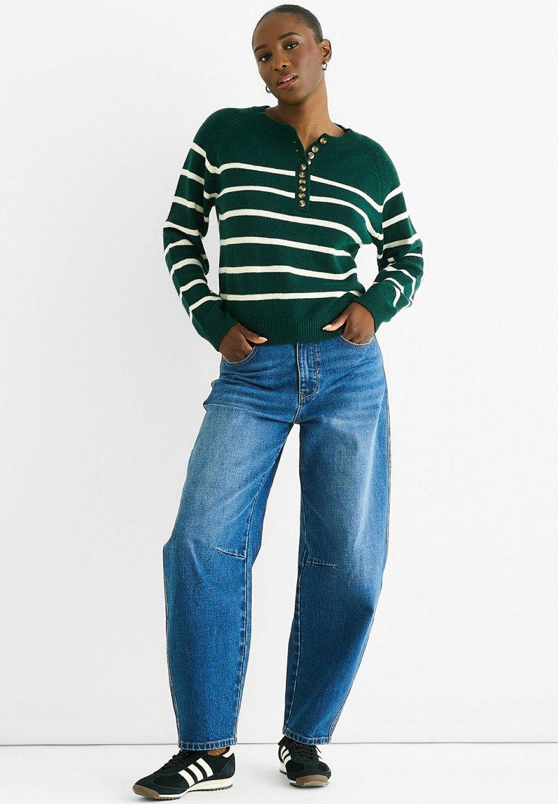 Green and white striped knit sweater with a henley neck and button detail, paired with loose blue jeans and black sneakers.
