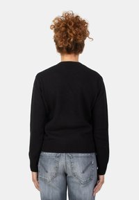 Maglione nero con orlo e polsini a coste, caratterizzato da un collo rotondo e una texture liscia, abbinato a jeans grigi chiari con dettagli sulle tasche.