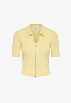 Sárga bordázott rövid ujjú galléros felső mély V-kivágással és elülső cipzárral. Strukturált gallérral és testhez álló kialakítással rendelkezik.