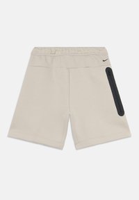 Beige athletic shorts with an elastic waistband, side zipper pocket, and black accents. Made from soft, stretchy fabric for comfort.