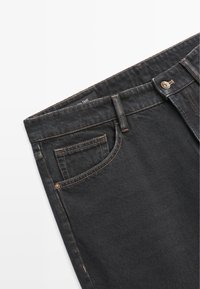 Jean en denim noir avec des coutures oranges, design à cinq poches et fermeture à bouton à l'avant. Présente une étiquette sur la ceinture.